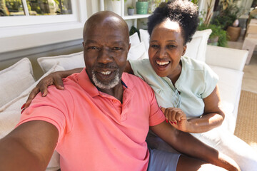 Portrait of smiling senior african american couple making video call in sunny living room