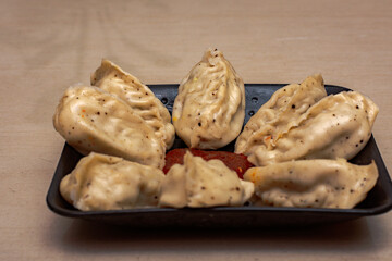Delicious fresh home made chicken steam momo a Tibetan Traditional dish Momo stuffed with chicken and then steamed cooked and served with red garlic sauce on a black plate. selective focus.