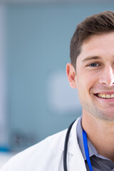 Unaltered portrait of happy caucasian male doctor smiling in hospital corridor, with copy space