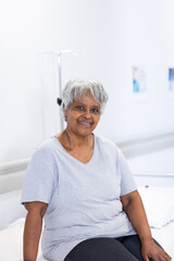 Unaltered portrait of happy senior biracial female patient on hospital bed smiling, with copy space