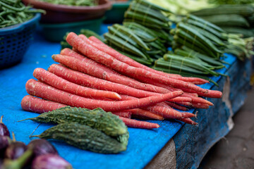 Thin carrots lying on tablecloth next to other vegetables at Goa bazaar in India. Sale of veggies in street market.