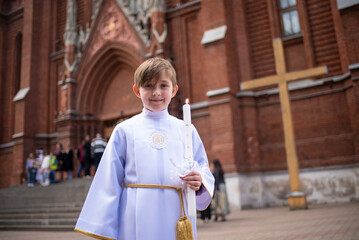 a child in white traditional festive clothes with a saint before his first communion stands near a...