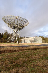 Photo of a radio satellite in a grass field next to a hangar against an overcast sky