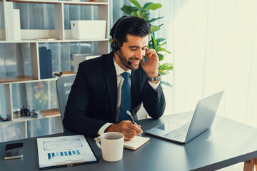 Male call center operator or telesales representative siting at his office desk wearing headset and engaged in conversation with client providing customer service support or making a sale. fervent - obrazy, fototapety, plakaty
