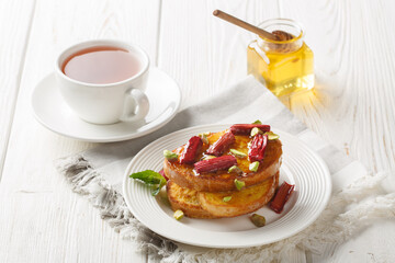 Breakfast french toast with baked rhubarb, pistachios, honey and tea close-up on a wooden table. Horizontal