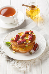 Delicious French toast with baked rhubarb, pistachios and honey close-up on a plate on a wooden table. Vertical