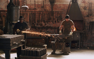 Hammer, anvil and sparks with men working in a forge for metal work manufacturing or production. Industry, welding and trade with a young male blacksmith in a workshop, plant or industrial foundry