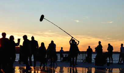 silhouette of people recording movie with sound recorder man holding boom microphone against dusk sky in Zadar, Croatia