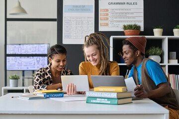 Multiethnic group of students watching online lesson together on tablet pc while sitting at table with books in classroom