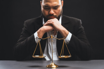 Focus golden scale balance with burred background of lawyer in black suit sit on his office desk, symbol of legal justice and integrity, balanced and ethical decision in court of law equility - obrazy, fototapety, plakaty
