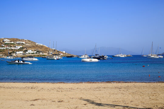 Ornos in Mykonos, Greece is a small coastal town with lots of small coves, luxury boats and yachts are moored on the bright blue calm sea.