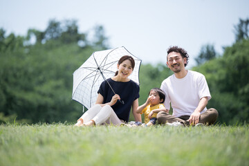 Asian family relaxing on park lawn with mother under parasol Relaxing on leisure seat Copy space available　looking at camera © kapinon