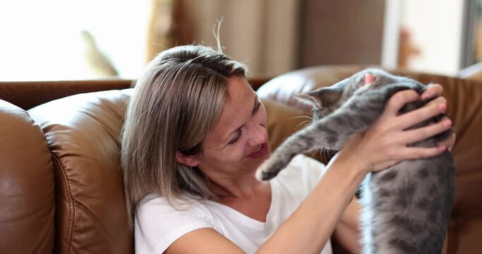 Portrait of beautiful woman holding small cat from happiness at home. Attractive woman sitting on sofa spending free time with pet in living room