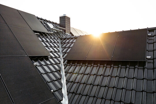 Solar panels on a dark tiled roof captured with a lens flare at sunrise