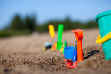 Fototapeta na wymiar Children's toys for playing on the sand. Plastic bucket and rake on the beach at sunset. The concept of summer, family holidays and vacations. Various plastic toys for children.