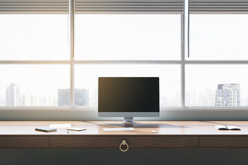 Clean office interior with panoramic windows and city view, empty mock up computer screen, furniture and sunlight. 3D Rendering.