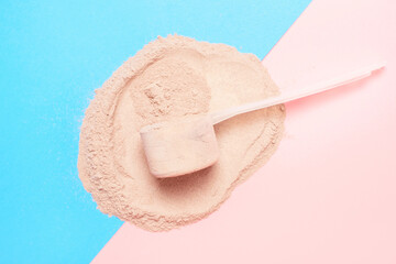 Scattered protein and measuring spoon on blue and pink background top view, concert of sports nutrition.