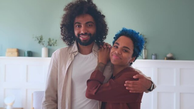 Young happy diverse couple middle eastern man and African American woman stand in embrace and with smile look at camera enjoying long awaited meeting romantic relationship, located in own apartment