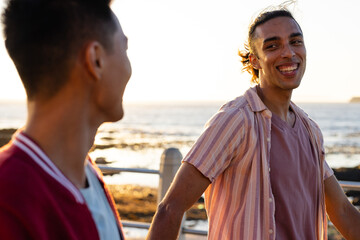 Happy biracial gay male couple walking and holding hands on promenade by the sea