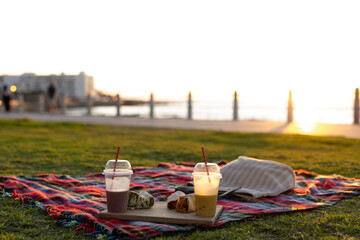 Close up of blanket with drinks and food on promenade by sea at sundown, with copy space