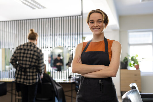 Portrait of smiling caucasian female hairdresser in black apron at hair salon, copy space
