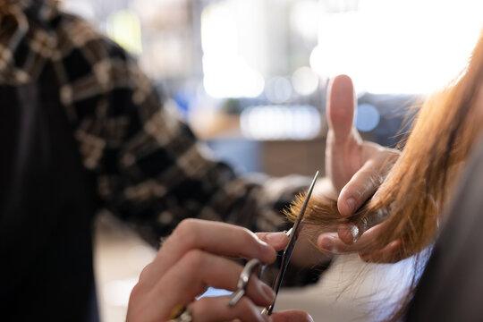 Hands of caucasian male hairdresser cutting ends of female customer's long hair at hair salon