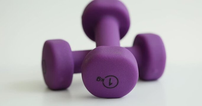 Purple dumbbells of 1 kg spinning on white background closeup 4k movie. Home female fitness concept