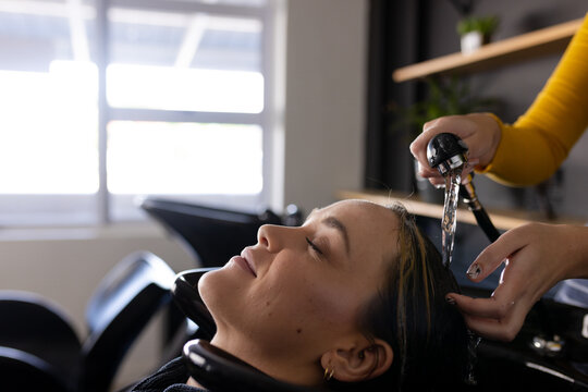 Hands of caucasian female hairdresser washing hair of relaxed, smiling female client at hair salon