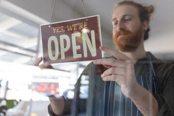 Happy caucasian male hairdresser turning sign to open on glass door of hair salon
