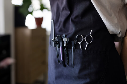 Midsection of caucasian male hairdresser wearing black apron with hairdressing tool in front pocket