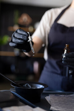 Midsection of caucasian female hairdresser in black apron and gloves preparing dye at hair salon