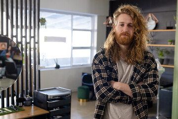Portrait of happy caucasian male customer with long curly red hair and beard at hair salon