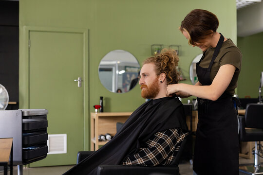 Focused caucasian female hairdresser cutting hair of male client in hair salon