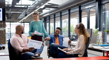 Happy diverse business people discussing work at meeting in creative office, unaltered