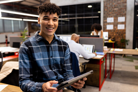 Portrait of happy biracial businessman with tablet over diverse colleagues in office, unaltered