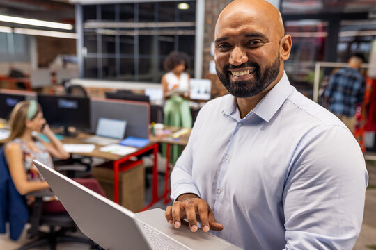 Portrait of happy african american businessman with laptop in office, unaltered