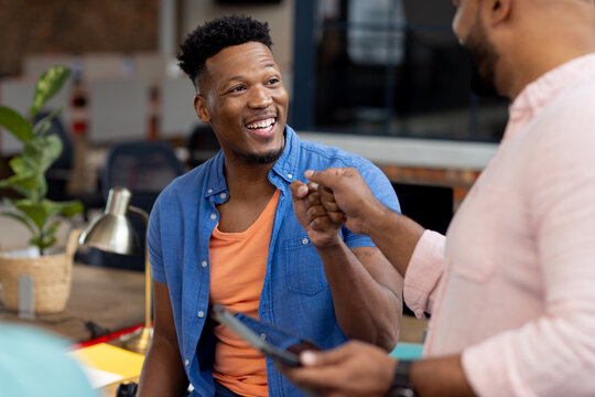 Happy diverse businessmen discussing work with tablet in creative office, unaltered