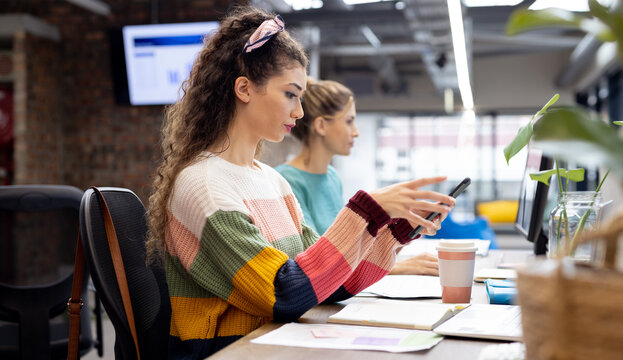 Busy diverse businesswomen working at desks using smartphone in creative office, unaltered