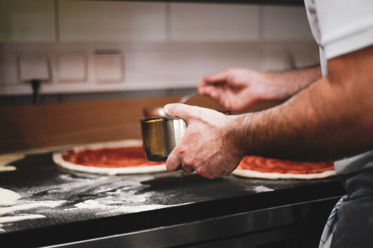 Chef hand adds tomato sauce to pizza dough in kitchen