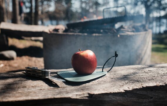 Apple on a camping chopping board and a pen knife by a campfire