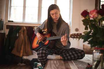 Asian person sits at home on wooden table playing guitar
