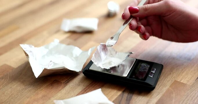 Hand pouring cocaine powder on foil on scales closeup 4k movie slow motion. Sale of drugs concept