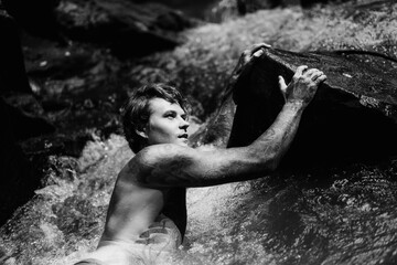 Young tattooed man swims in a mountain river in Bali.