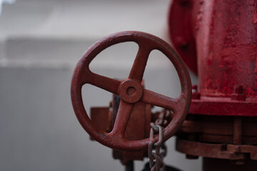 Water flows through a red pipe with a valve that can be opened or close with a red wheel. In the background is the white wall of a building.