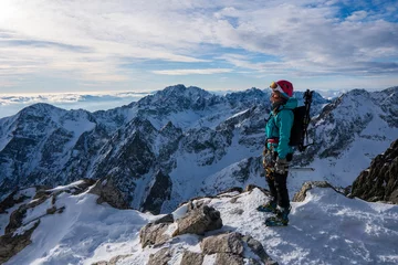 Foto op Plexiglas Tatra Adventurous women hiker on top of a steep rocky cliff overlooking winter alpine like moutain landscape of High Tatras, Slovakia. Alpine mountain landscape covered with glaciers, snow and ice.