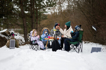 Family with three children in winter forest spending time together on a picnic.