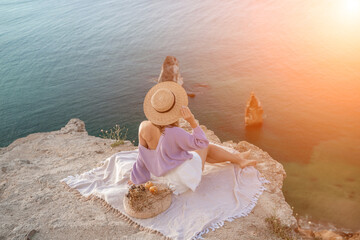 woman sea travel. photo of a beautiful woman with long blond hair in a pink shirt and denim shorts and a hat having a picnic on a hill overlooking the sea