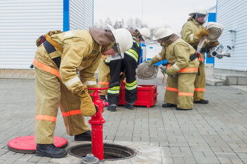 Fire brigade deploys equipment outside in open air and connects fire hydrant in well. Firefighting drills