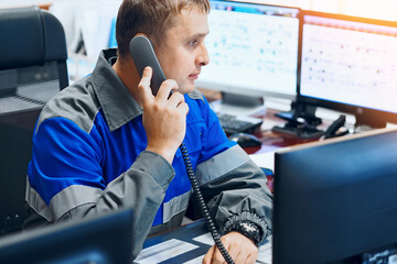 A dispatcher at an industrial enterprise sits in an office surrounded by monitors and talks on a...