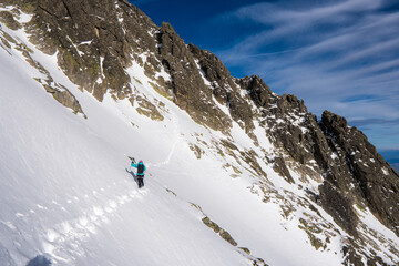 Fototapeta na wymiar Adventurous women hiker a steep rocky cliff overlooking winter alpine like moutain landscape of High Tatras, Slovakia. Alpine mountain landscape covered with glaciers, snow and ice. 